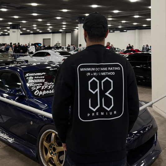 Person wearing a black hoodie with a logo and text, standing in a car showroom.