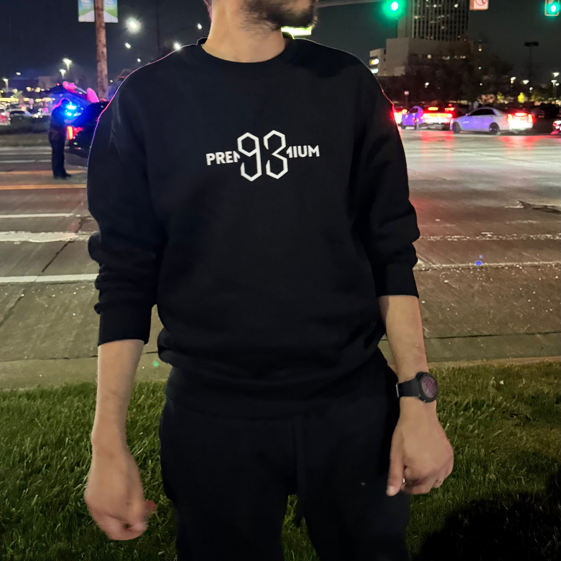 Man wearing a black sweatshirt with text standing on a street at night.