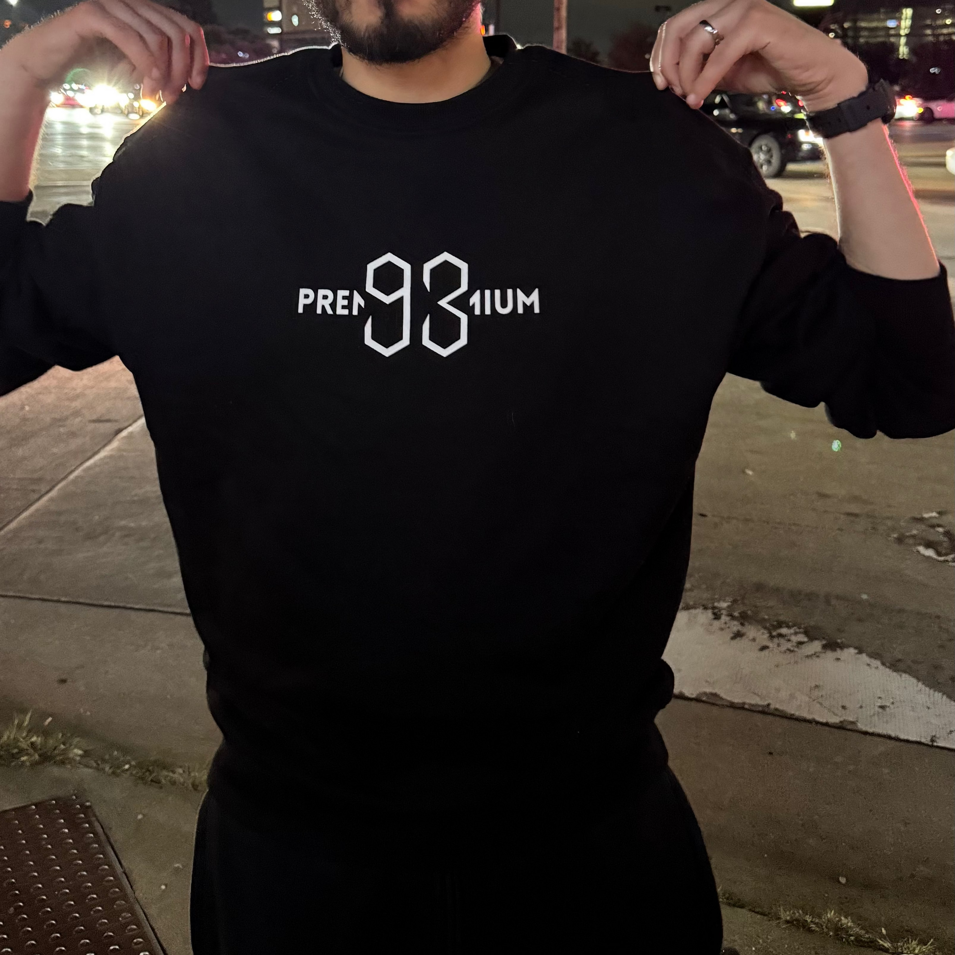Person wearing a black sweatshirt with 'PREMIUM' logo at night.