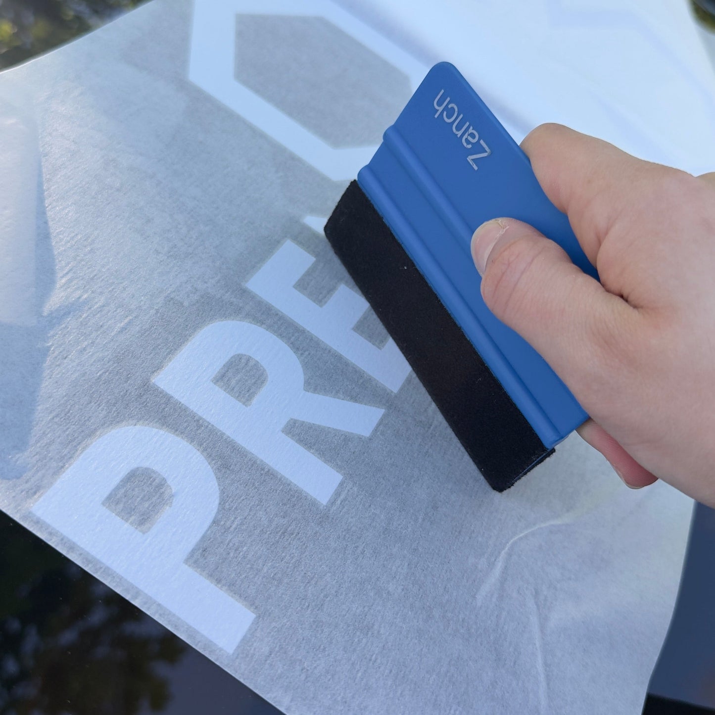 Person applying a car window film with a squeegee on a car window.
