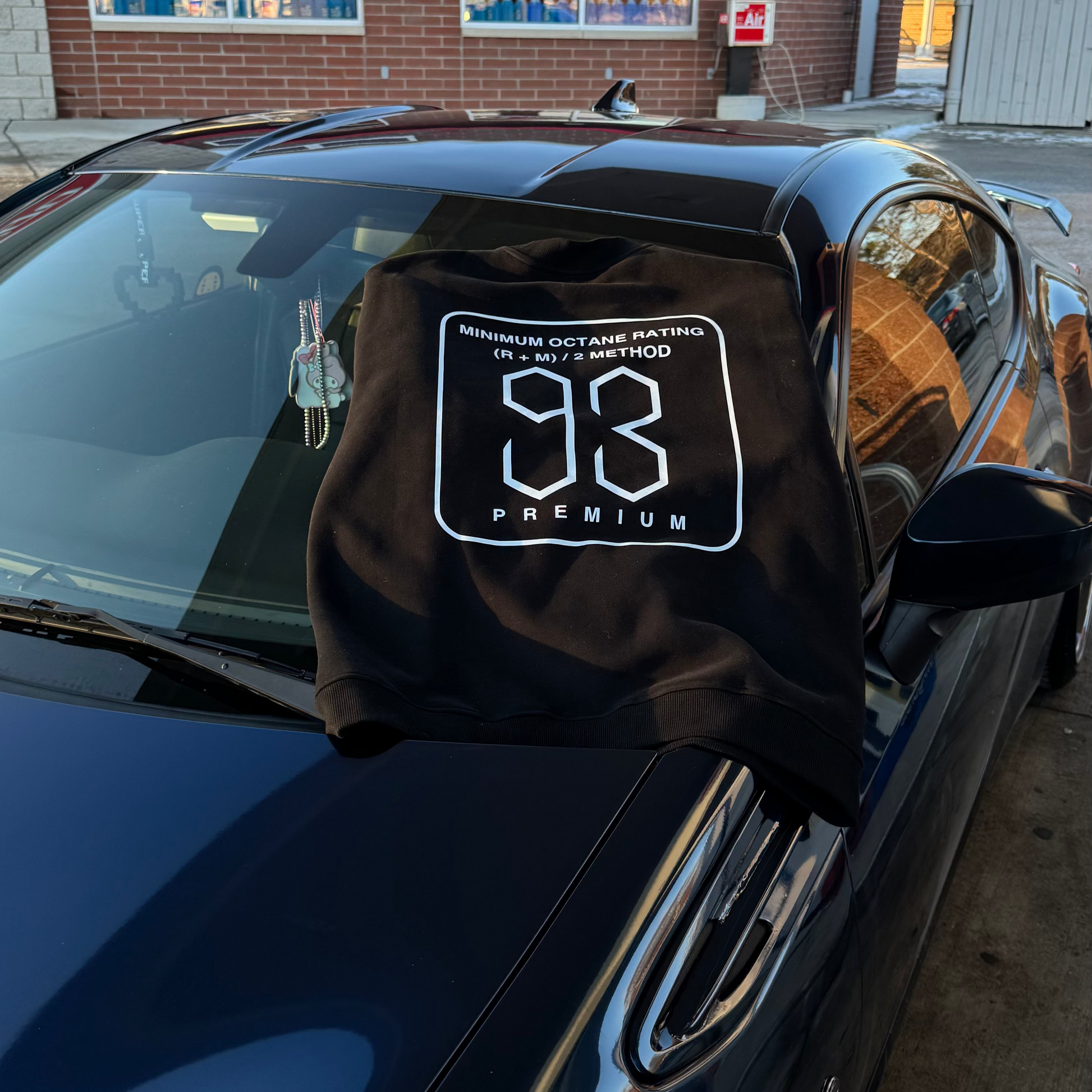 Black car cover with a logo on a black car in front of a brick building.