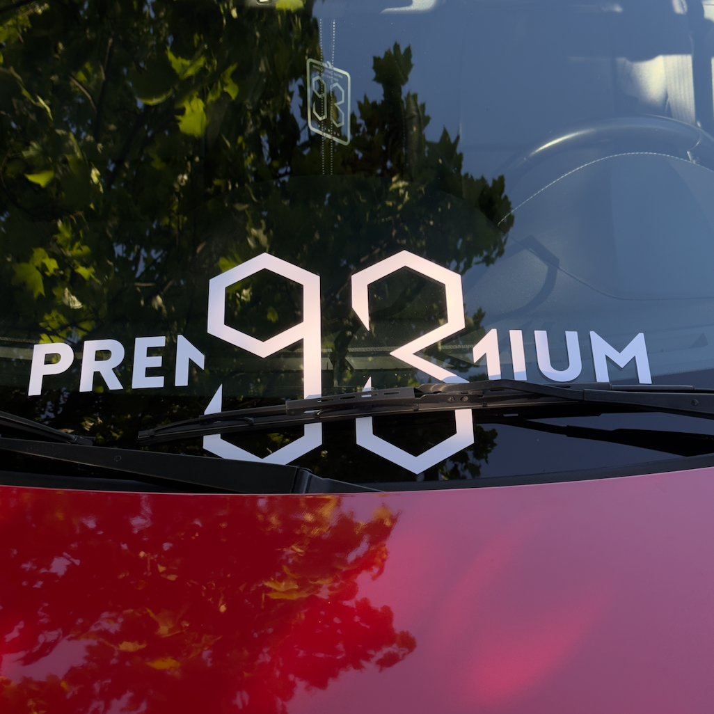 Car window with 'PREMIUM 93' decal and tree reflection